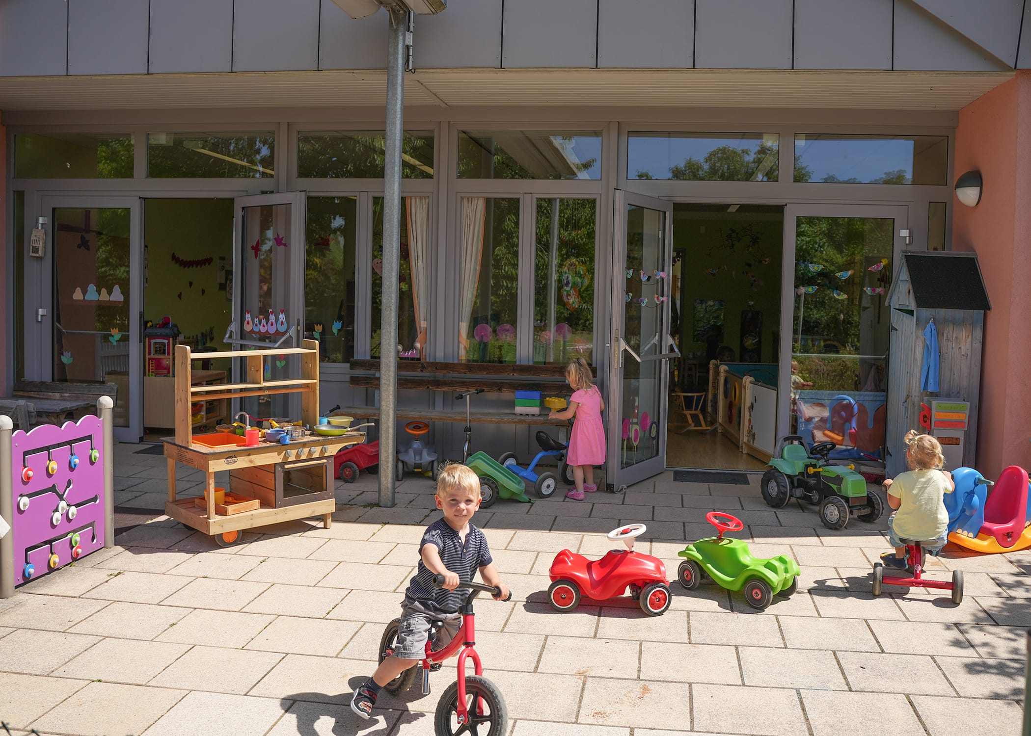 Raumbilder (30) Drei Kinder spielen draußen mit Laufrad und Dreirad